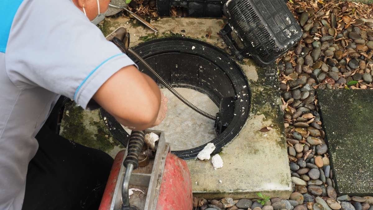 Professional plumber using an auger machine to repair a clogged grease trap and maintain a sewage system