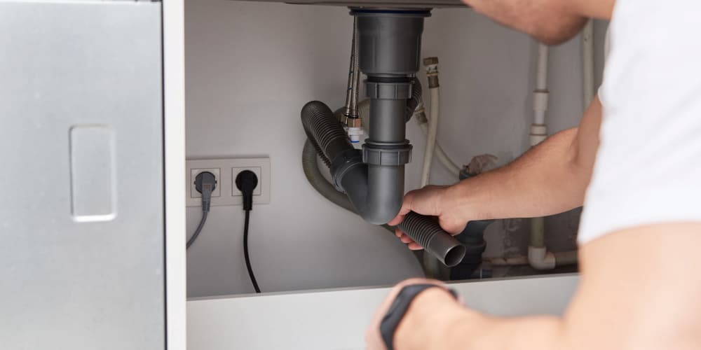Professional plumber working on a drain pipes under a kitchen sink.