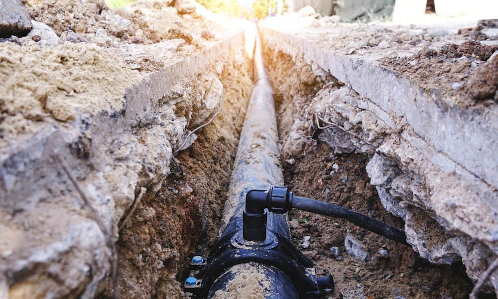Close-up of a water pipe installed in a narrow trench surrounded by soil and rocks.