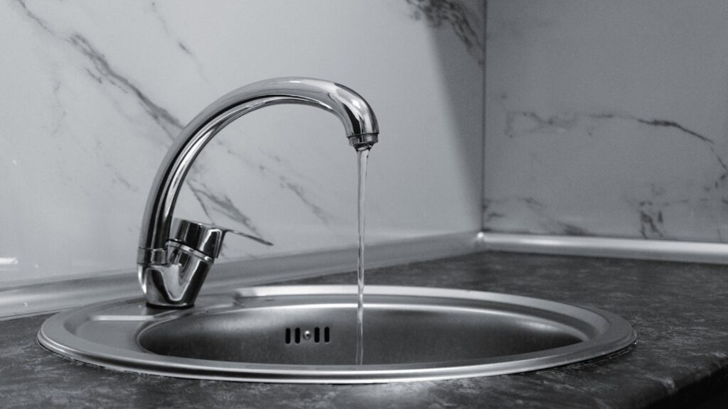 Modern chrome kitchen faucet with running water on marble countertop