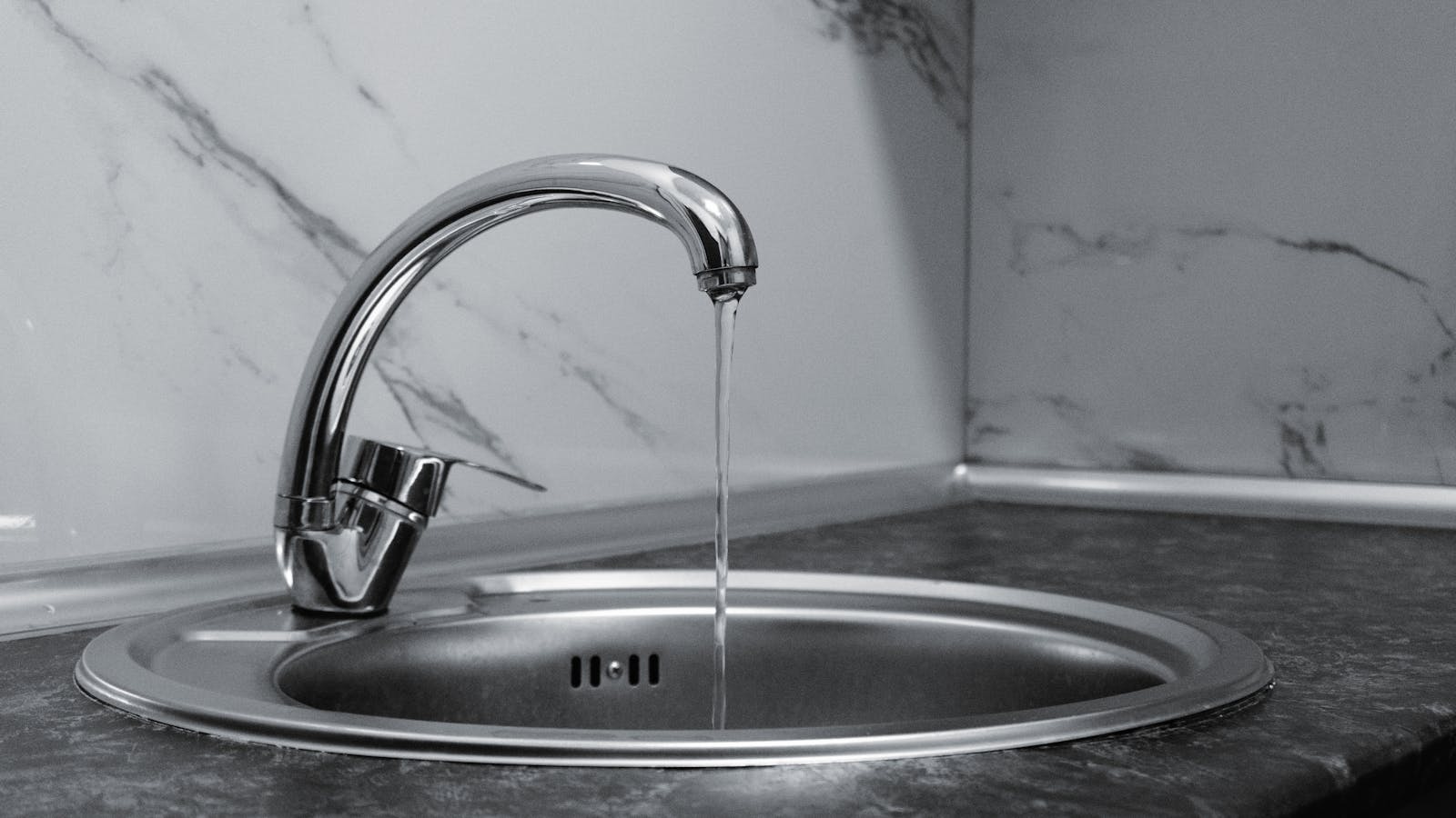 Modern chrome kitchen faucet with running water on marble countertop