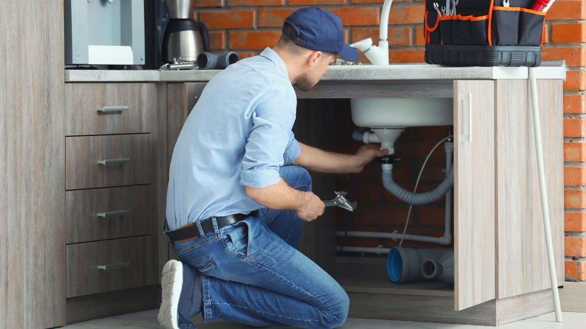 plumber kneels on the floor fixing the drain pipes