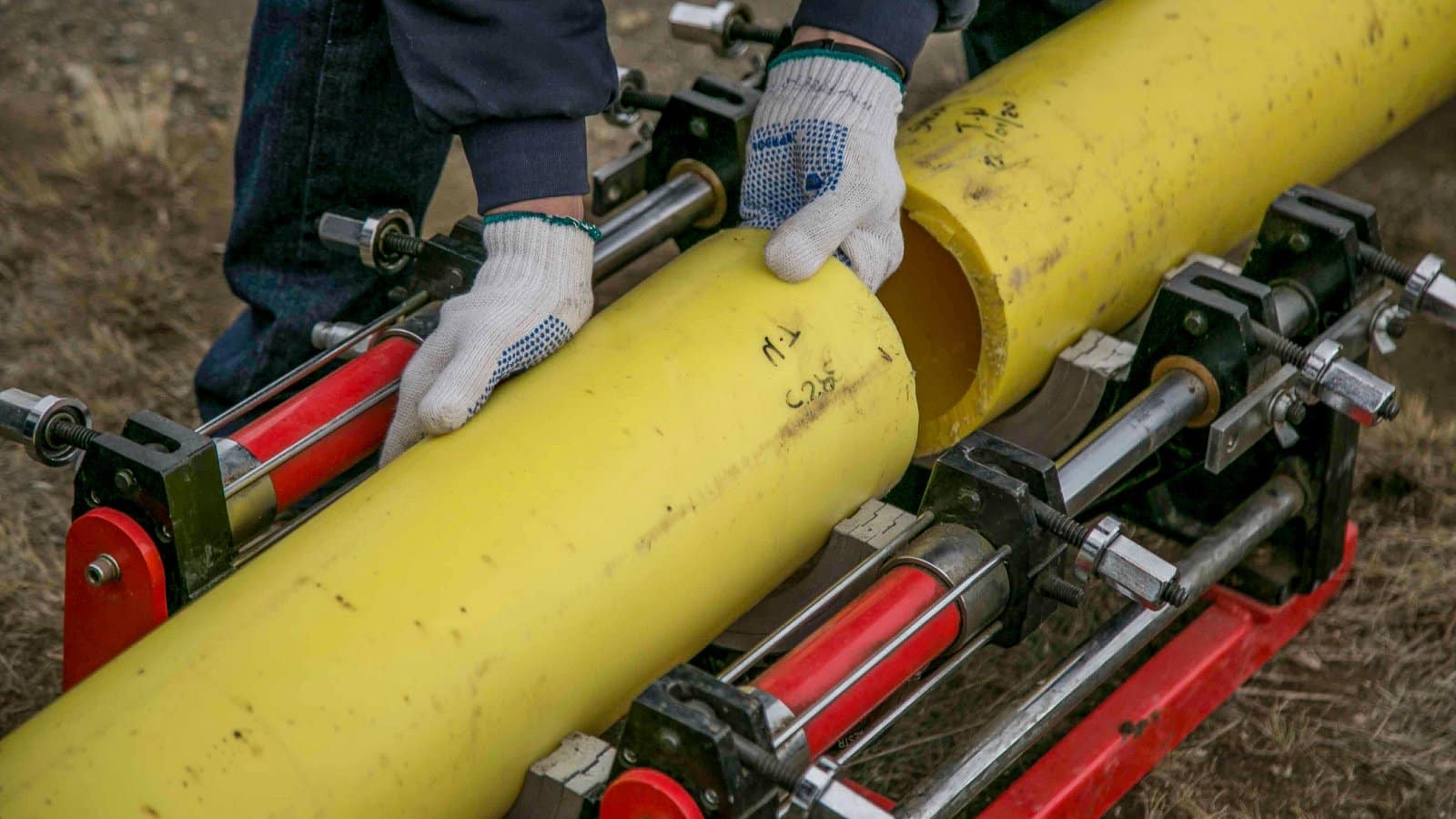Close-up view of a worker using equipment to install yellow pipes outdoors, focusing on hands and tools.