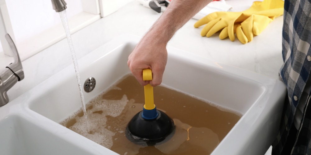 A person plunges a clogged kitchen sink