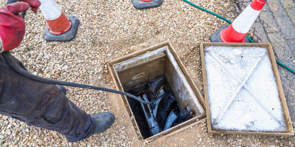 A worker feeds a thick black cable into an open square drain access hatch