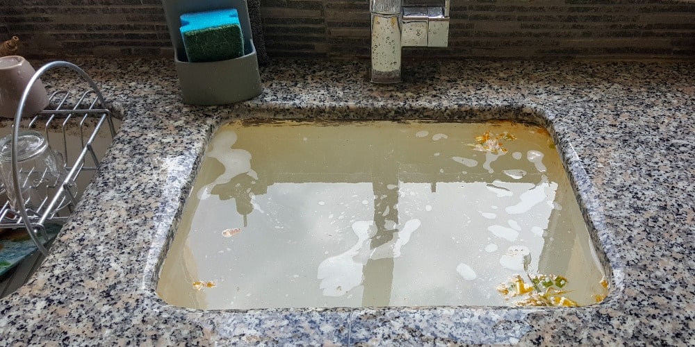 kitchen sink filled to the brim with dirty, standing soapy water