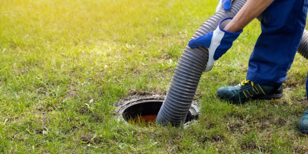 A worker wearing blue gloves guides a thick, ribbed suction hose