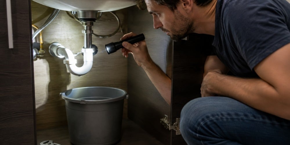 homeowner crouching under a bathroom sink