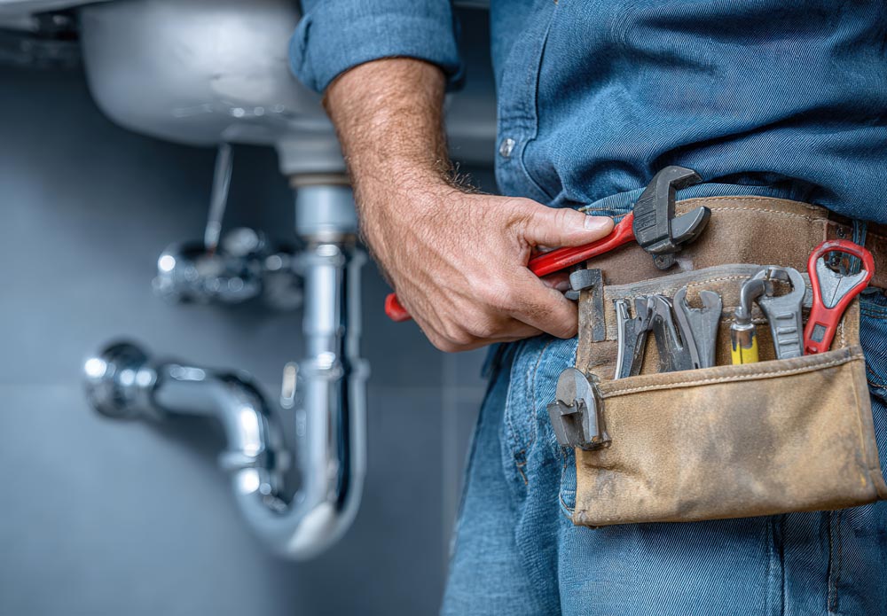 male plumber wearing blue shirt holds adjustable wrench
